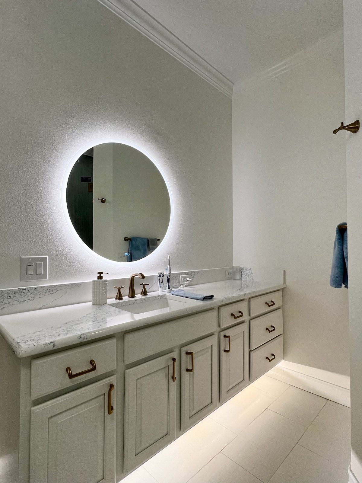 Long vanity with backlit round mirror and stone counter